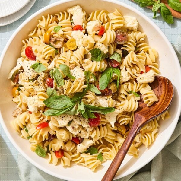 White bowl filled with Caprese pasta salad topped with fresh basil, tomatoes, and mozzarella.