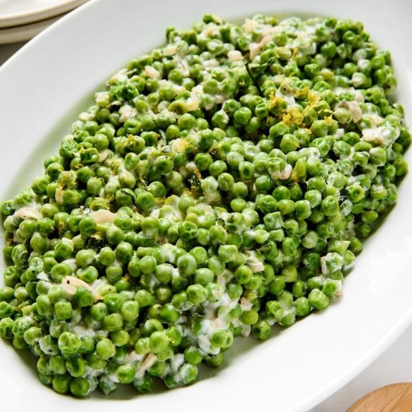White platter filled with creamed peas with lemon yogurt sauce on top.