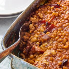 Green pan with baked beans with spoon scooping out a serving.