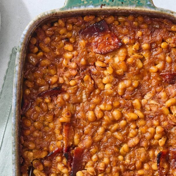 Bluish green pan filled with cooked homemade baked beans with pieces of bacon on top.