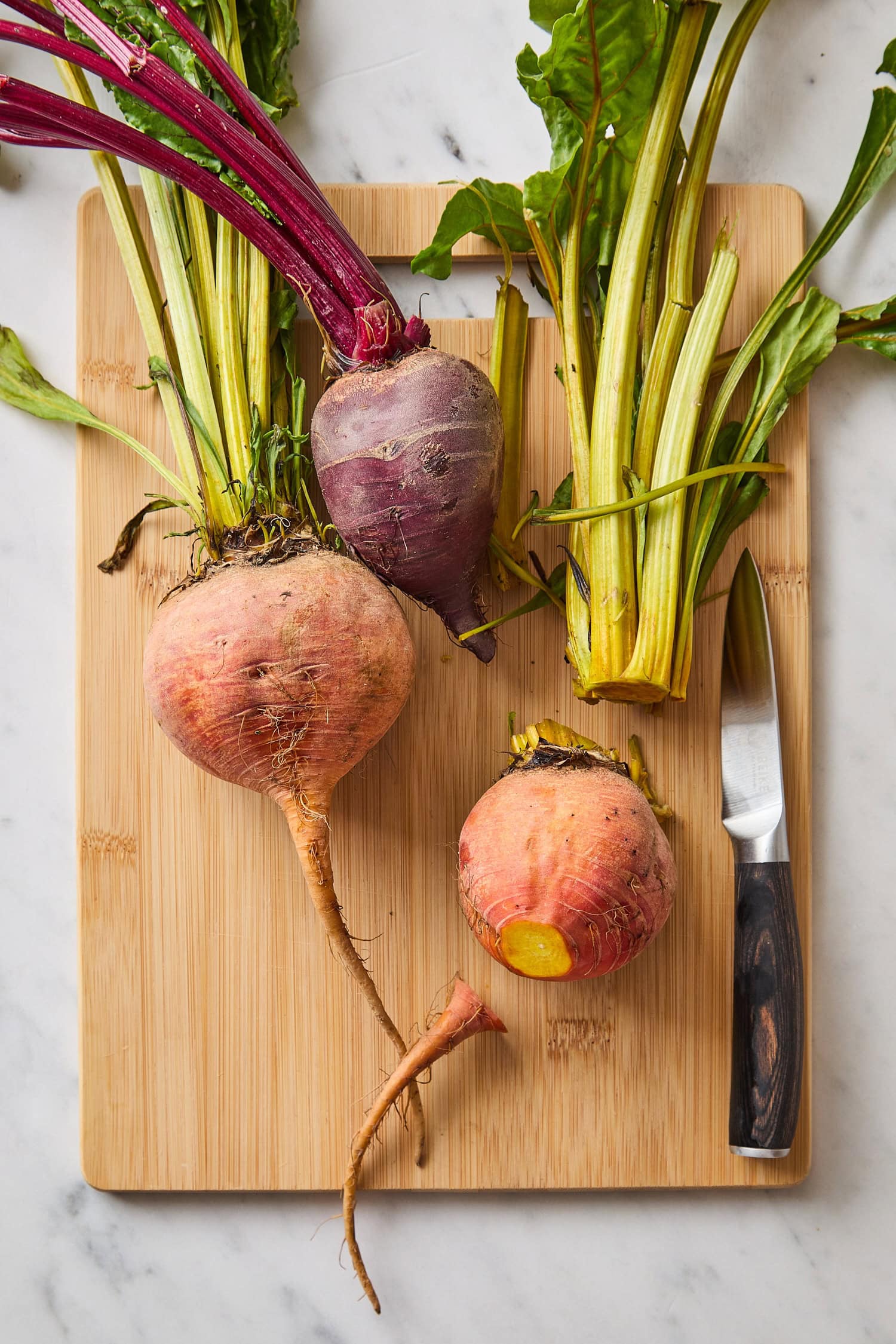 Wooden cutting board with beets being prepared for roasting.