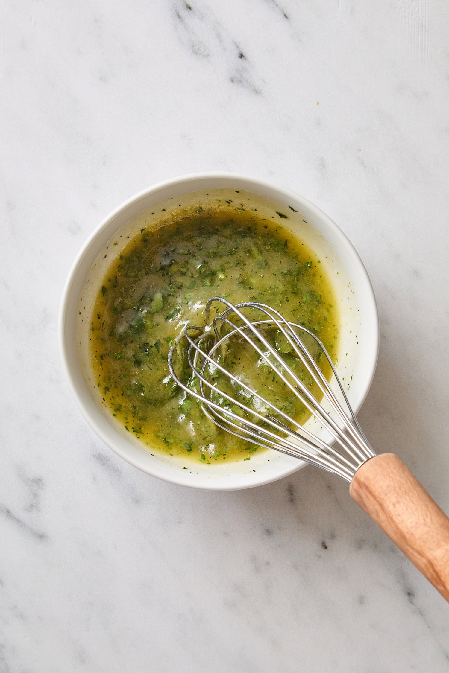 White bowl with green colored dressing being whisked.