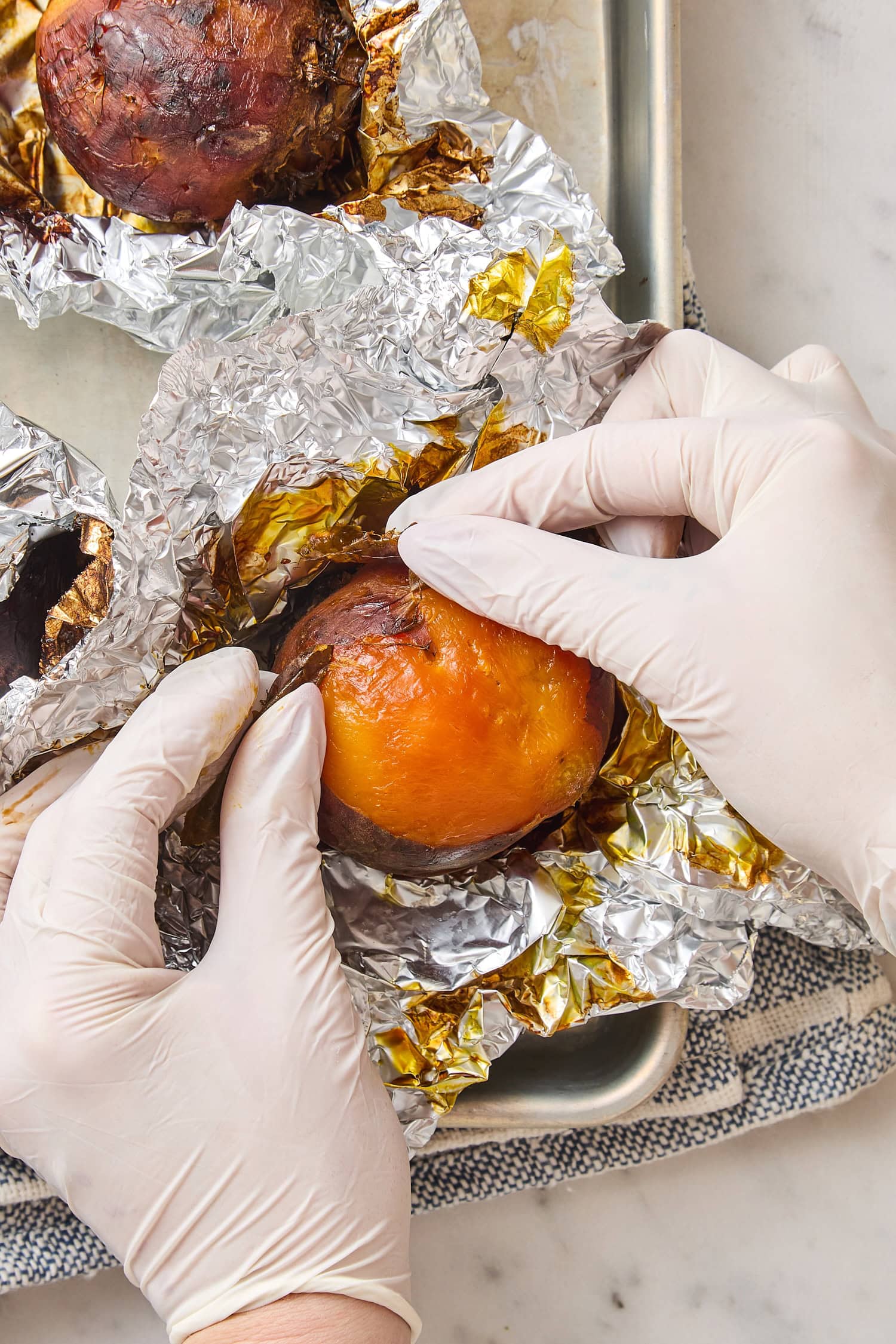 Hands peeling off skin from beets after being roasted.