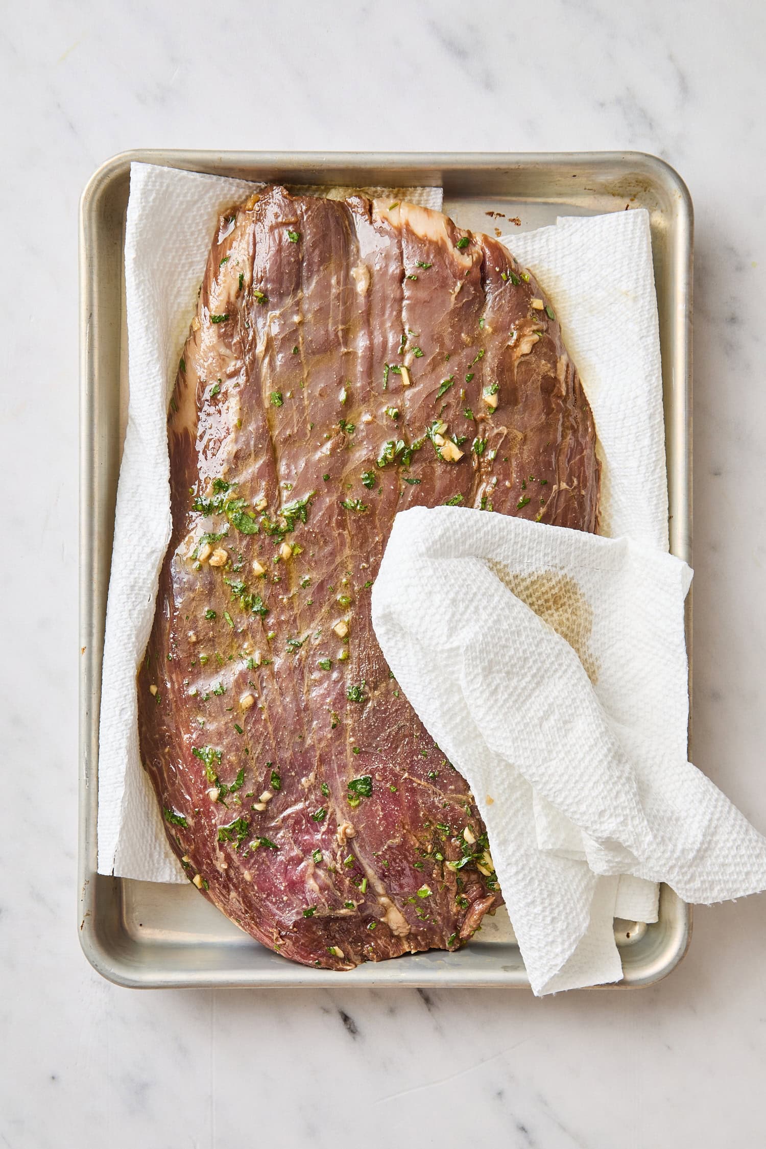 Raw marinated steak with paper towel dabbing off excess.