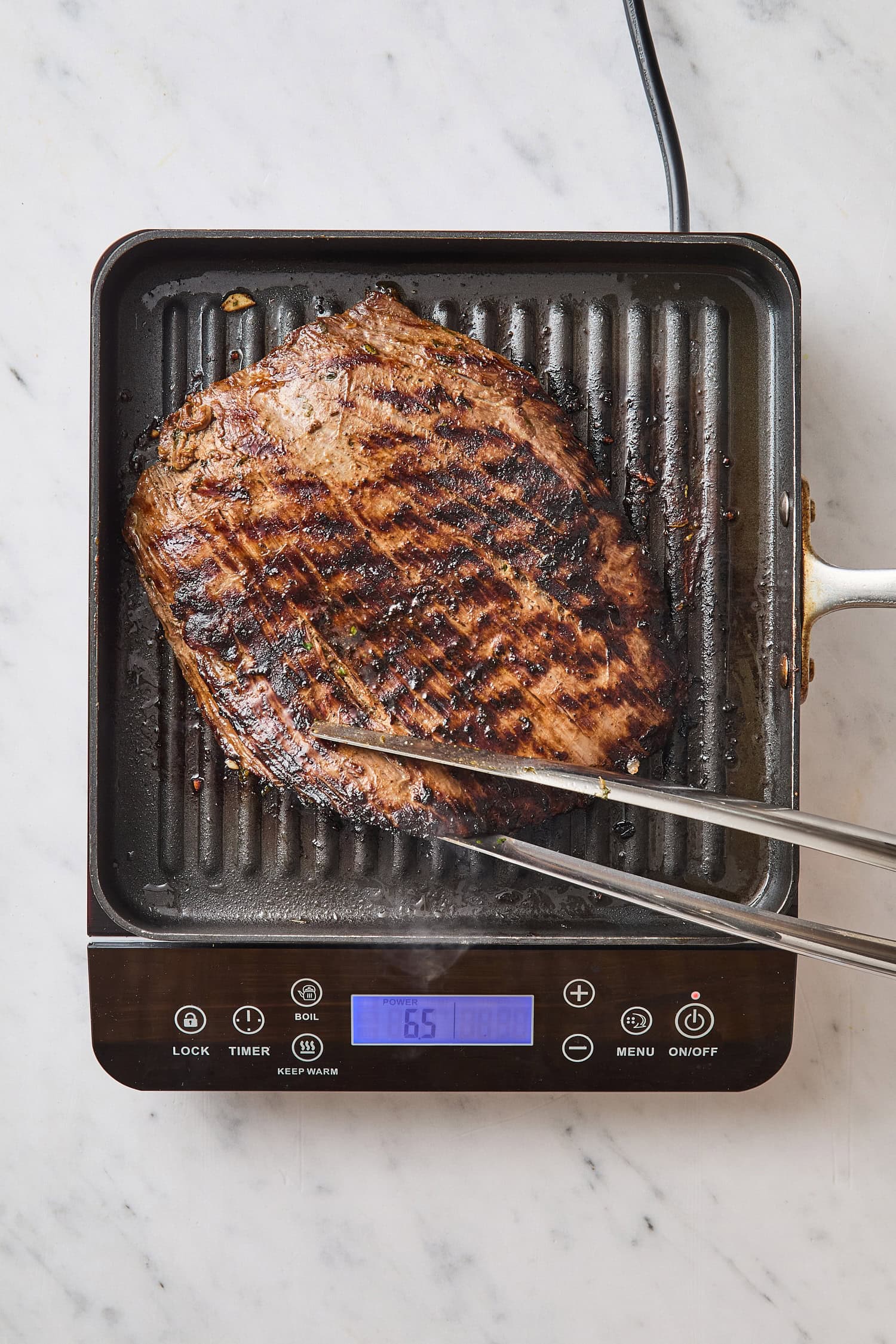 Tongs flipping over grilled steak on grill pan.