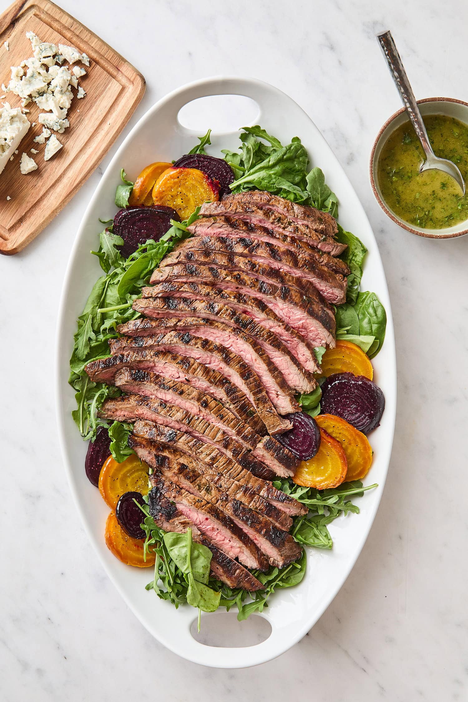 White platter with assembly of steak and beet salad on spinach and arugula.