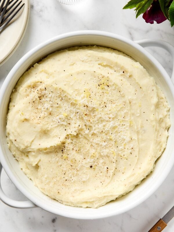 Lemon ricotta mashed potatoes with black pepper and lemon zest on top sitting on white marble surface.