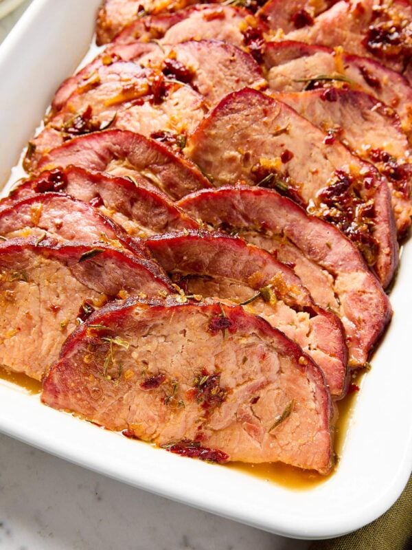 Slices of glazed ham sitting in a baking dish after cooking.