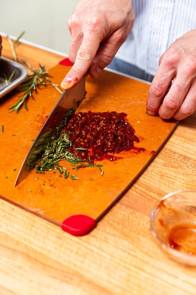 Chopping up rosemary and chipotle adobo peppers for a ham glaze.