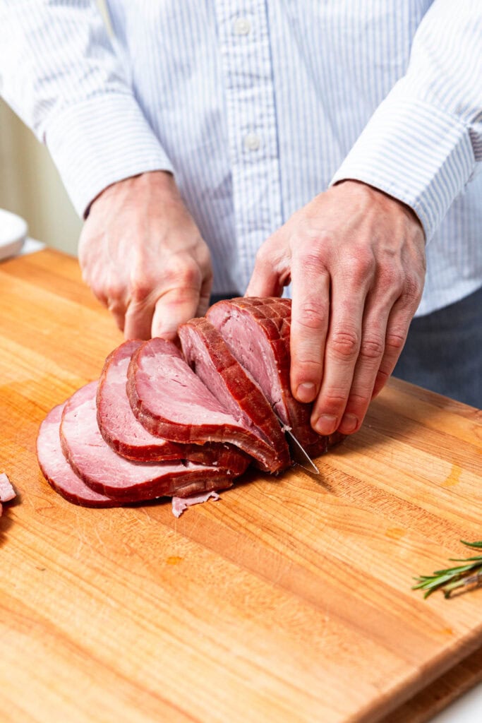 Slicing ham quarters into smaller slices.