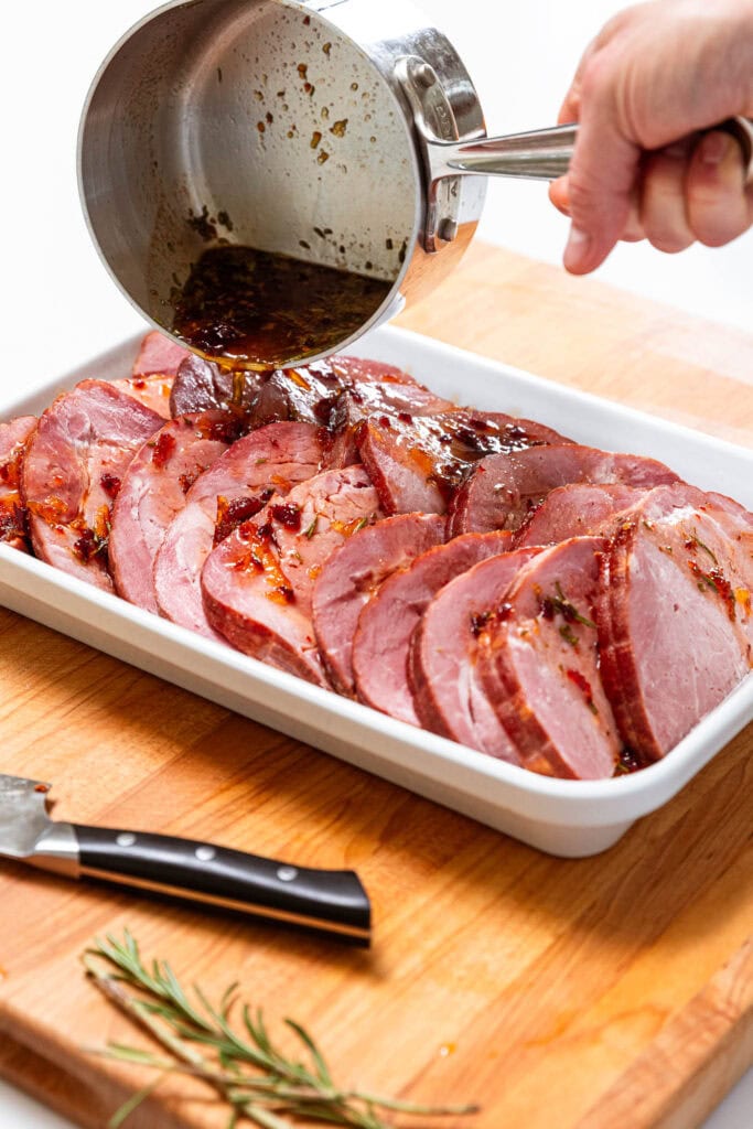 Pouring glaze over sliced ham in a baking dish.