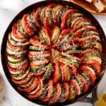 Black skillet with cooked ratatouille with Parmesan cheese on top.