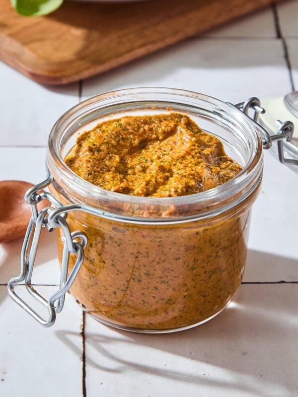 Orange colored arugula pesto in a jar with a spoon to the side.