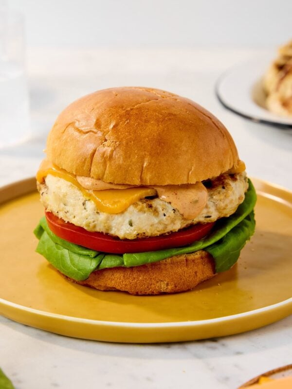 A chicken burger with lettuce, tomato, and sauce sits on a plate.