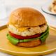 A chicken burger with lettuce, tomato, and sauce sits on a plate.