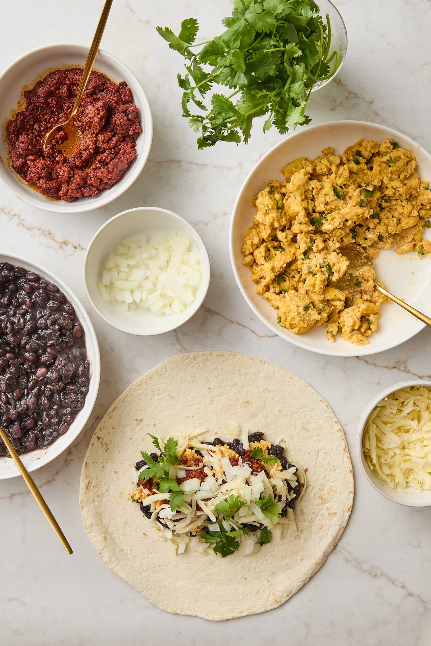 Surface with eggs, beans, chorizo, and cheese to make breakfast burritos.
