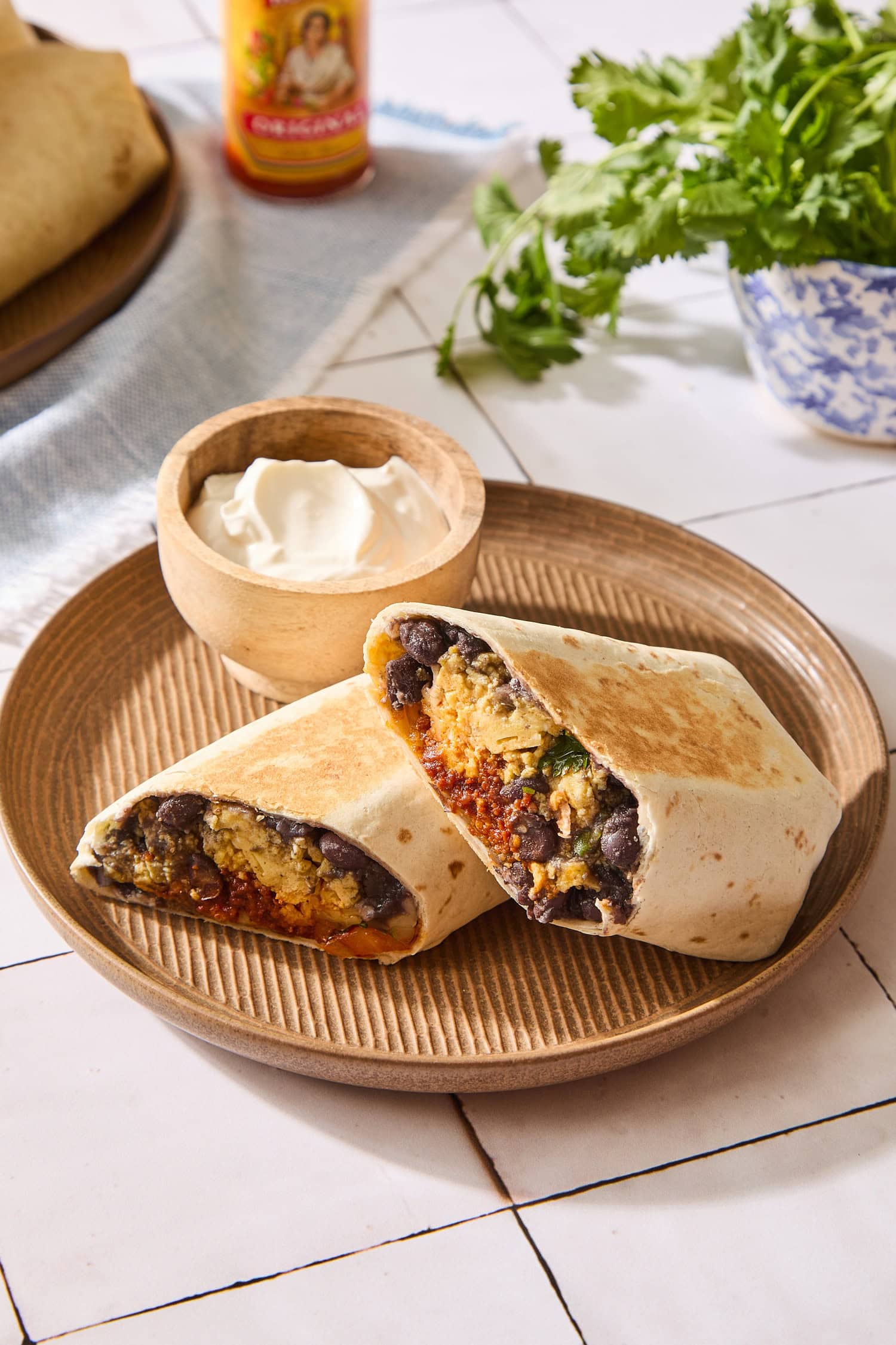 Burritos on a plate sliced in half with hot sauce in background.