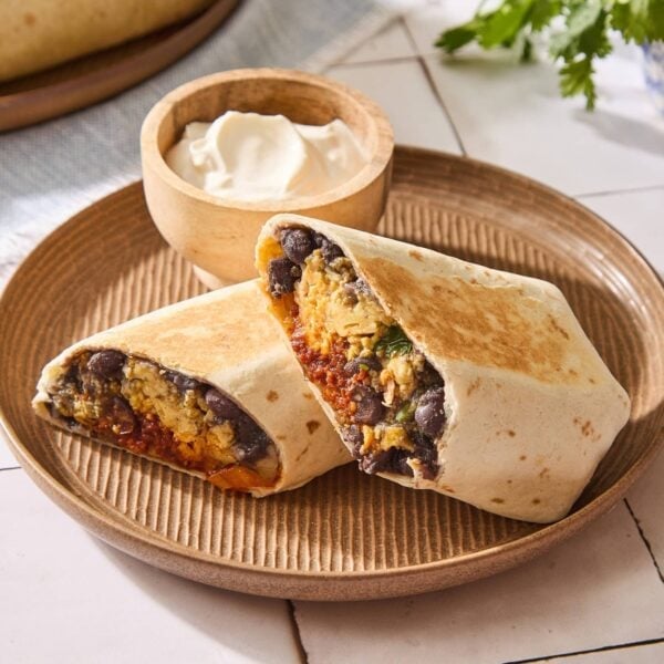 Tile surface with brown plate with chorizo breakfast burritos with sour cream.