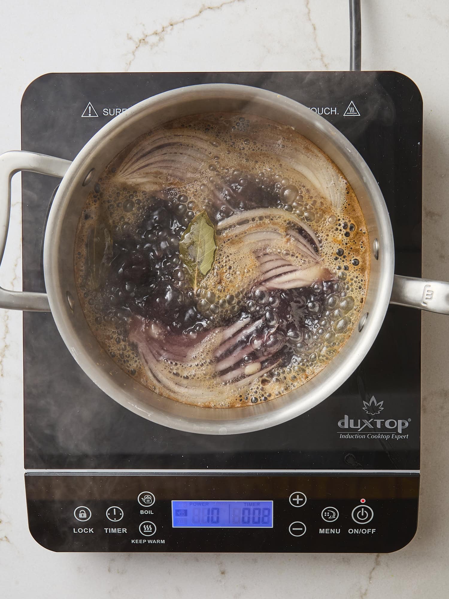 Hot plate with saucepan with cooking black beans with onion and herbs.