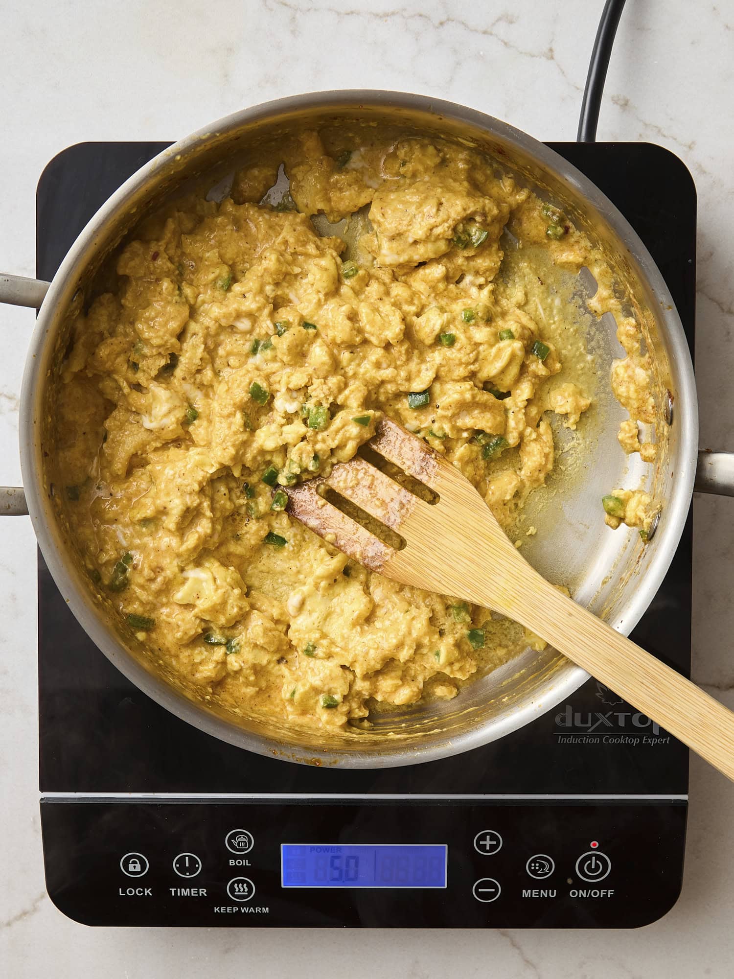 Scrambled eggs cooking in a pan on a hot plate.