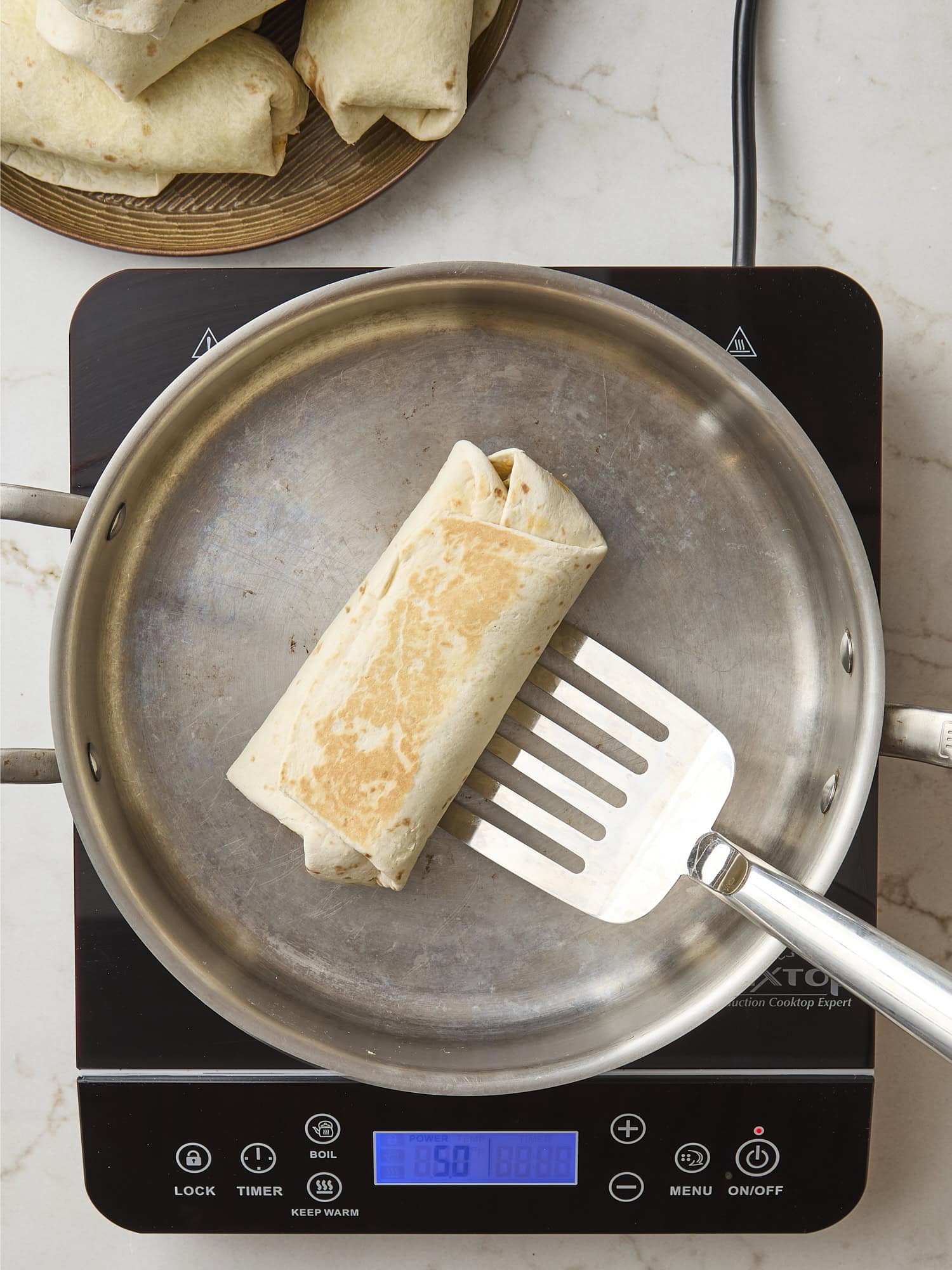 Browned and crisped breakfast burrito cooking in pan on hot plate.