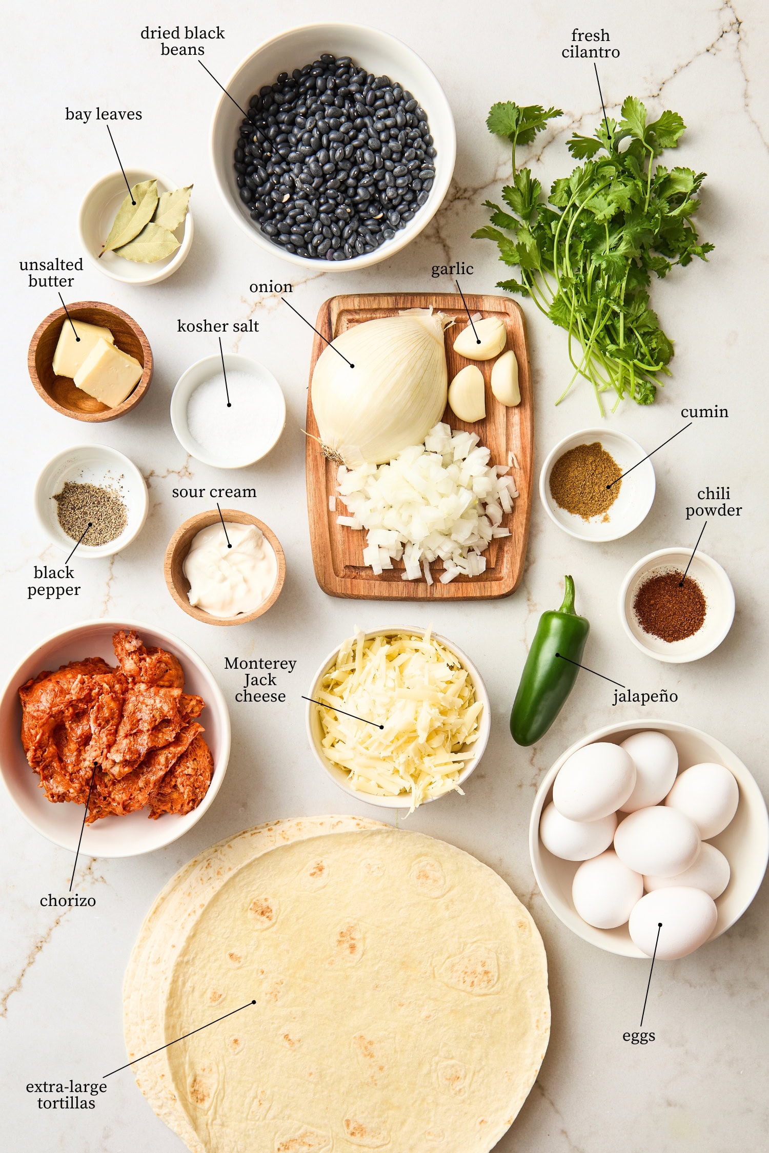 White surface with ingredients for chorizo breakfast burritos including meat, tortillas, eggs, and more.