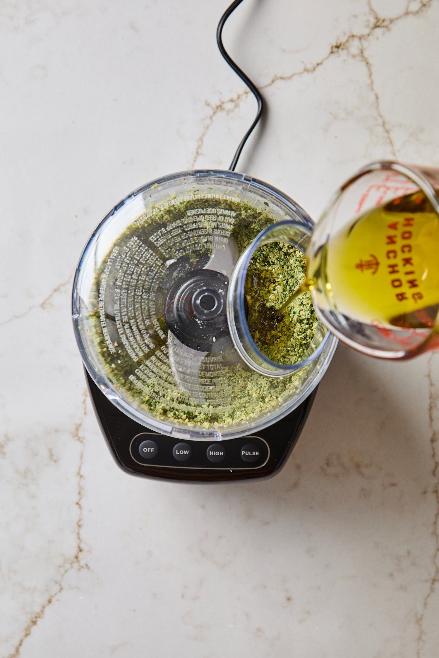 Olive oil being poured into a food processor for basil pesto recipe.