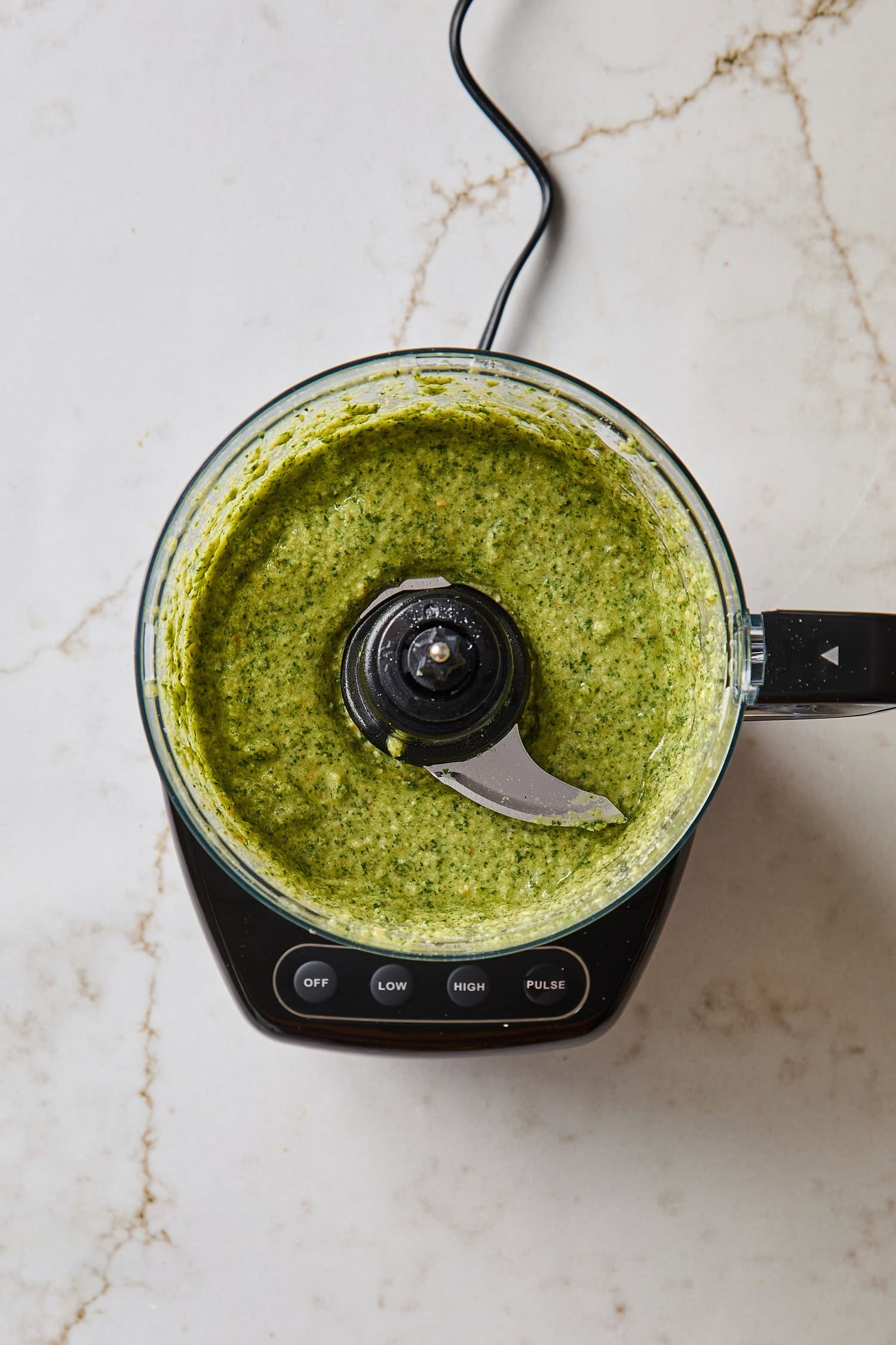 Food processor with bright green freshly-blended basil pesto.