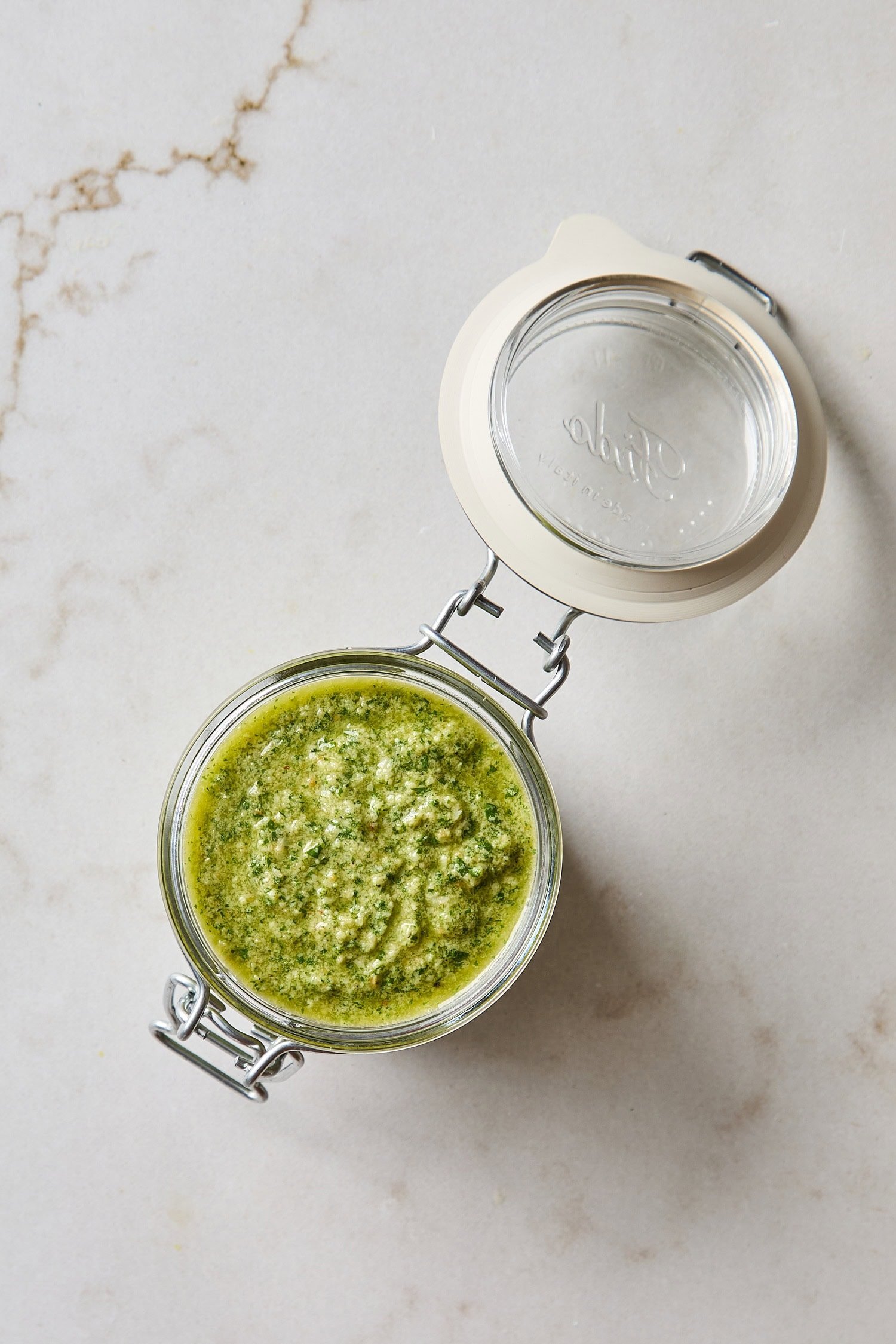 Canister of fresh basil pesto on white countertop before being stored.