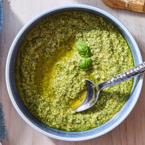 Blue bowl filled with green colored basil pesto with spoon resting in bowl.