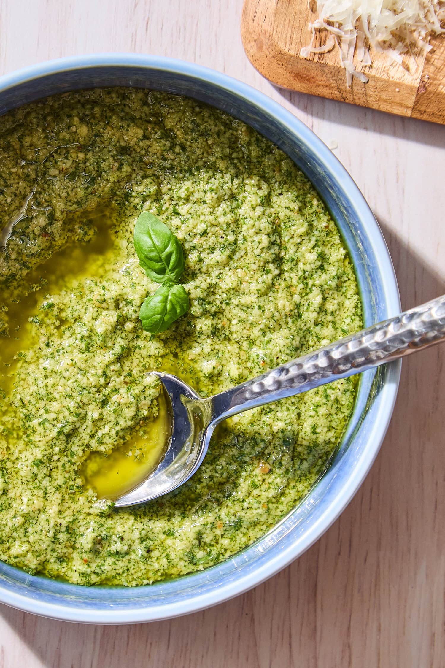 Blue bowl with spoon sitting in basil pesto with two small basil leaves.