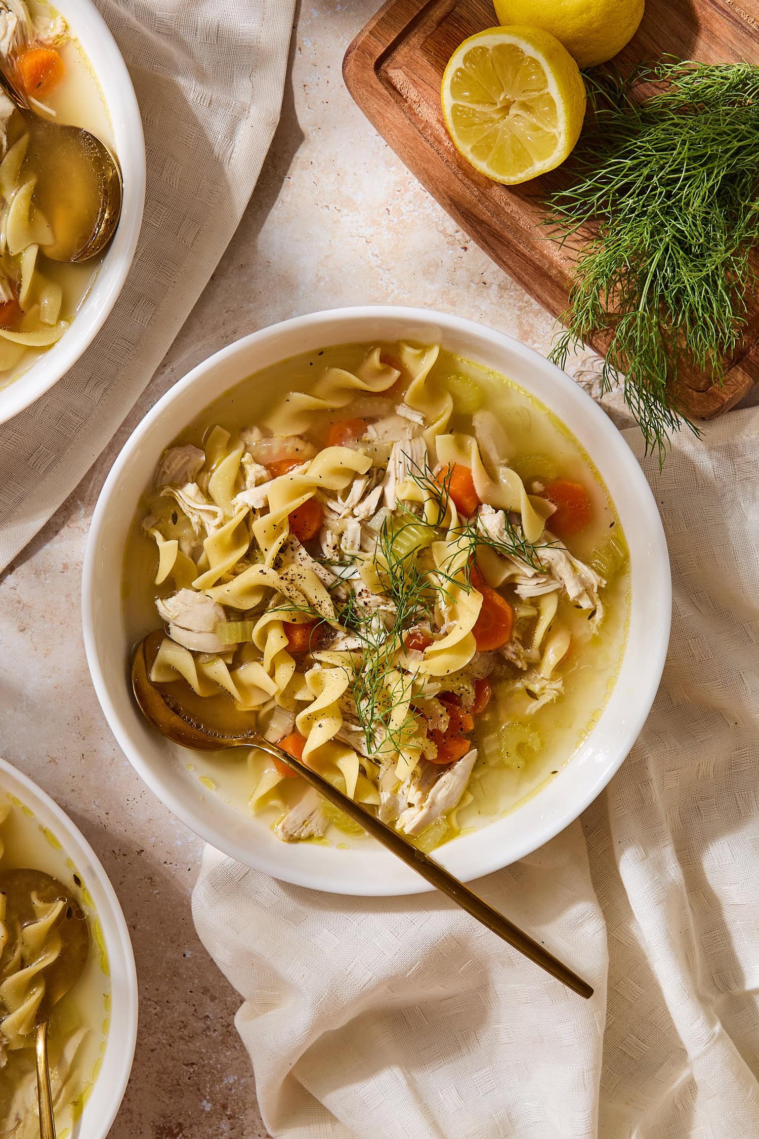 Bowl filled with homemade chicken noodle soup with spoon resting in bowl with carrots and fresh herbs on top.