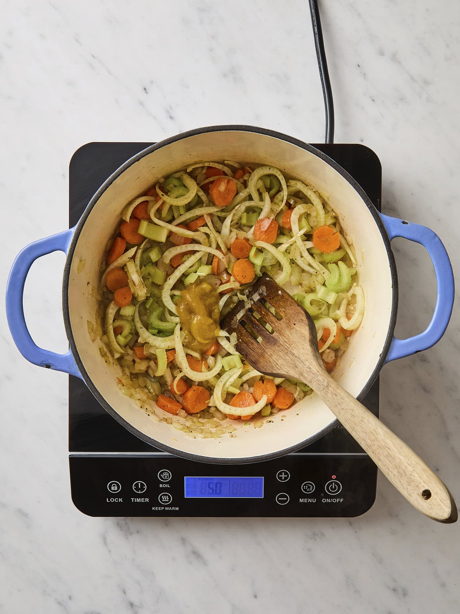 White marble surface with pot filled with cooking carrots, celery, and onion for soup.