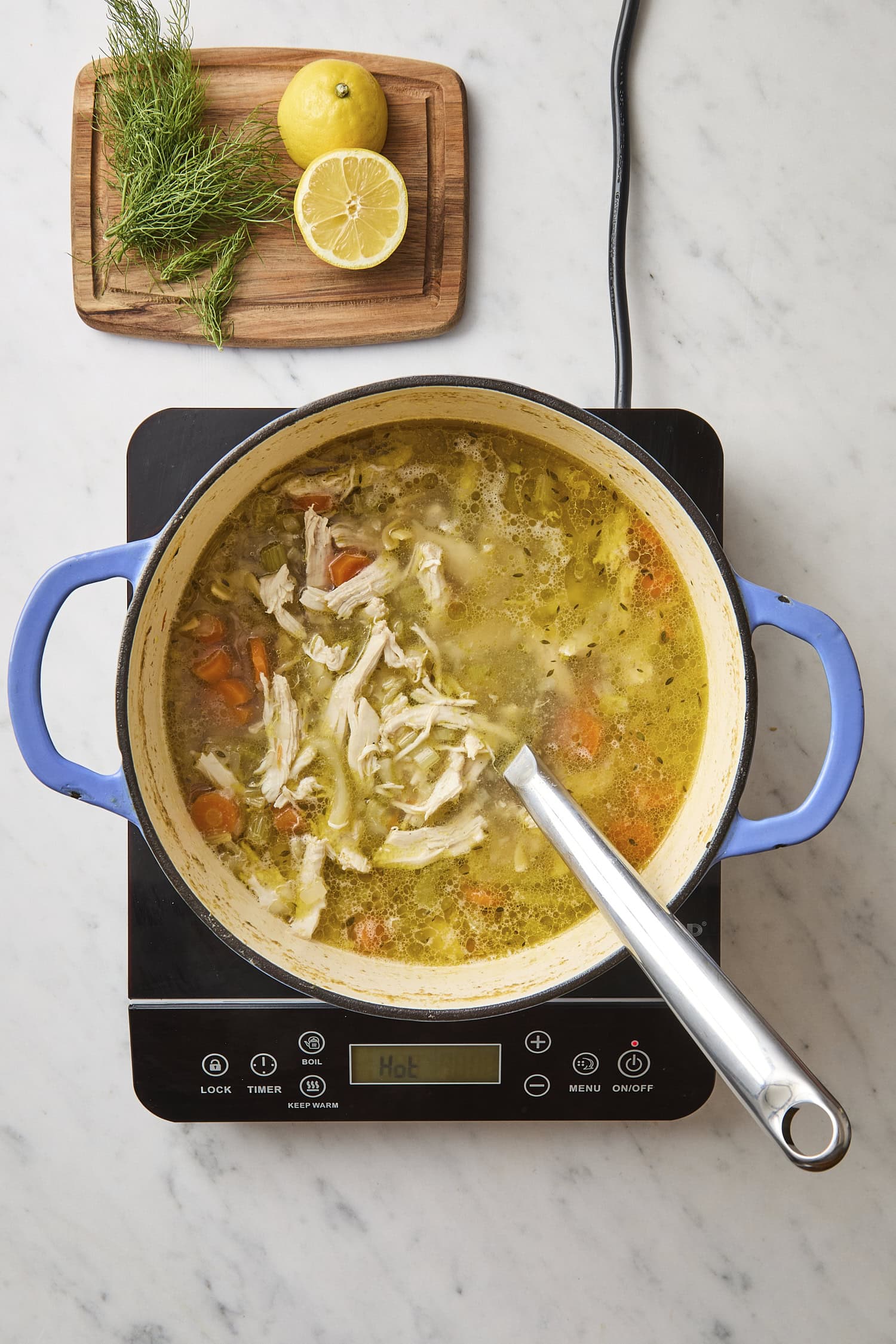 Pot filled with chicken noodle soup cooking on heat with lemon and herbs.