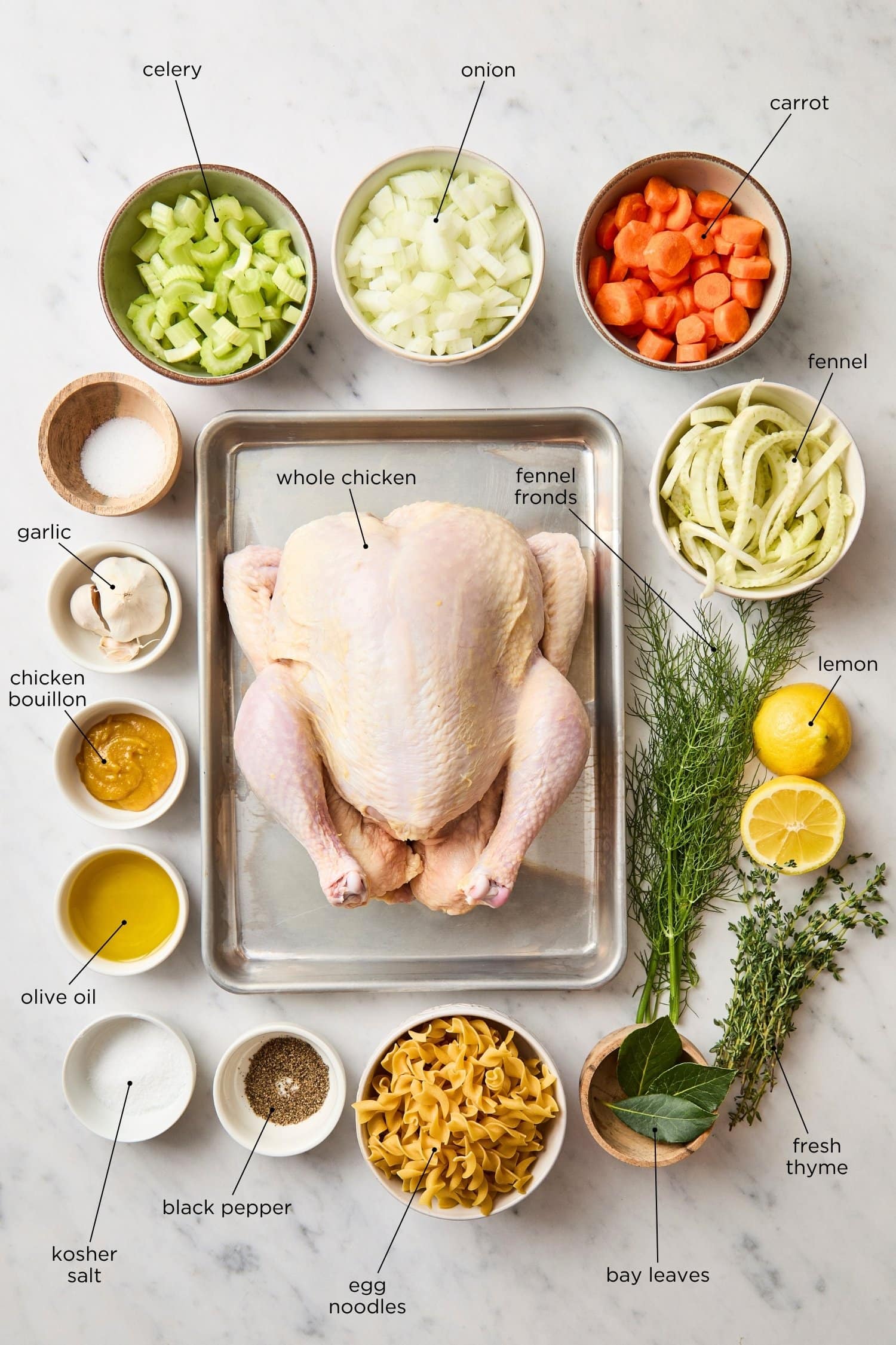 Marble surface with ingredients needed to make a homemade chicken noodle soup recipe.