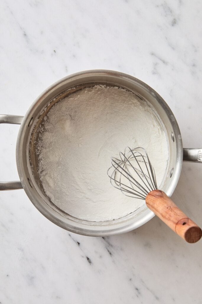Metal saucepan with sugar, salt, and cornstarch with a whisk.