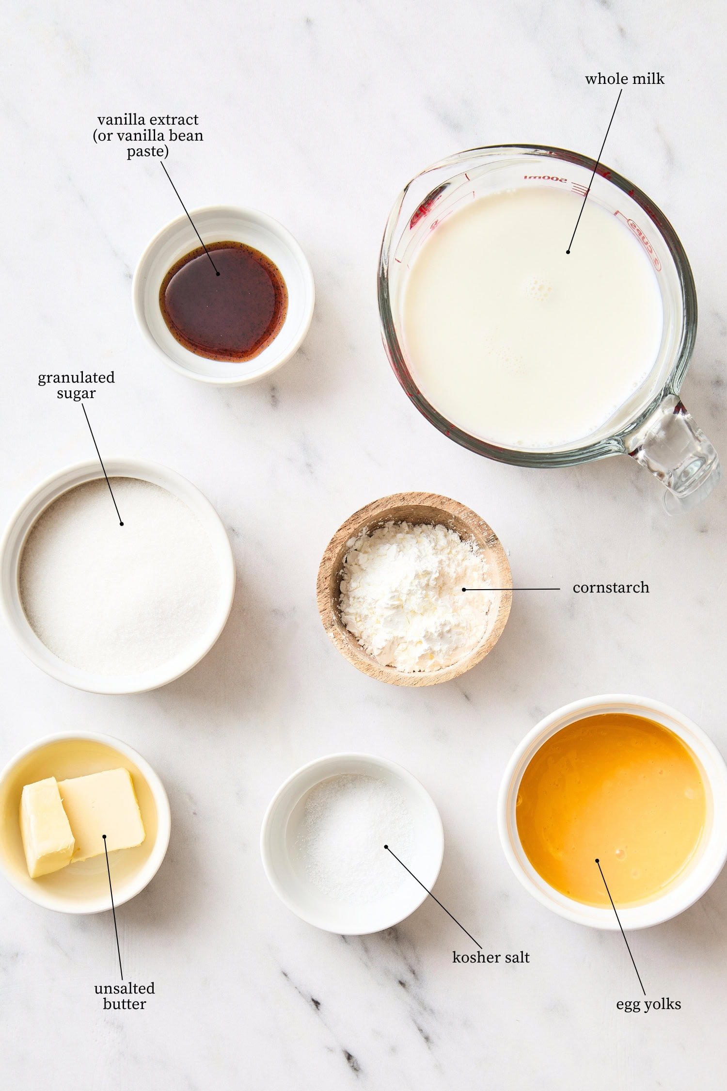 White marble surface filled with ingredients needed for vanilla pudding recipe.