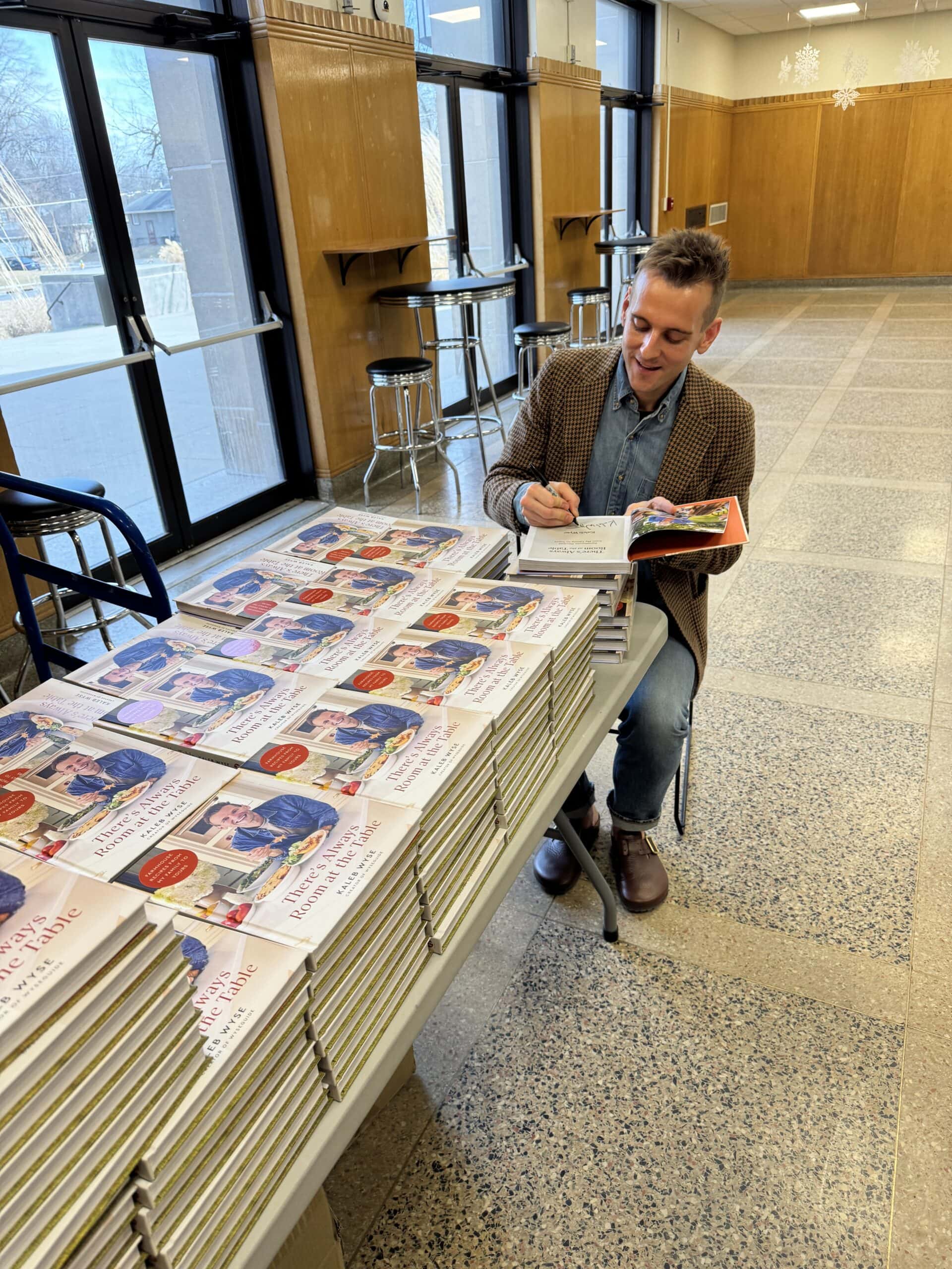 Kaleb Wyse signing copies of his cookbooks in a lobby.