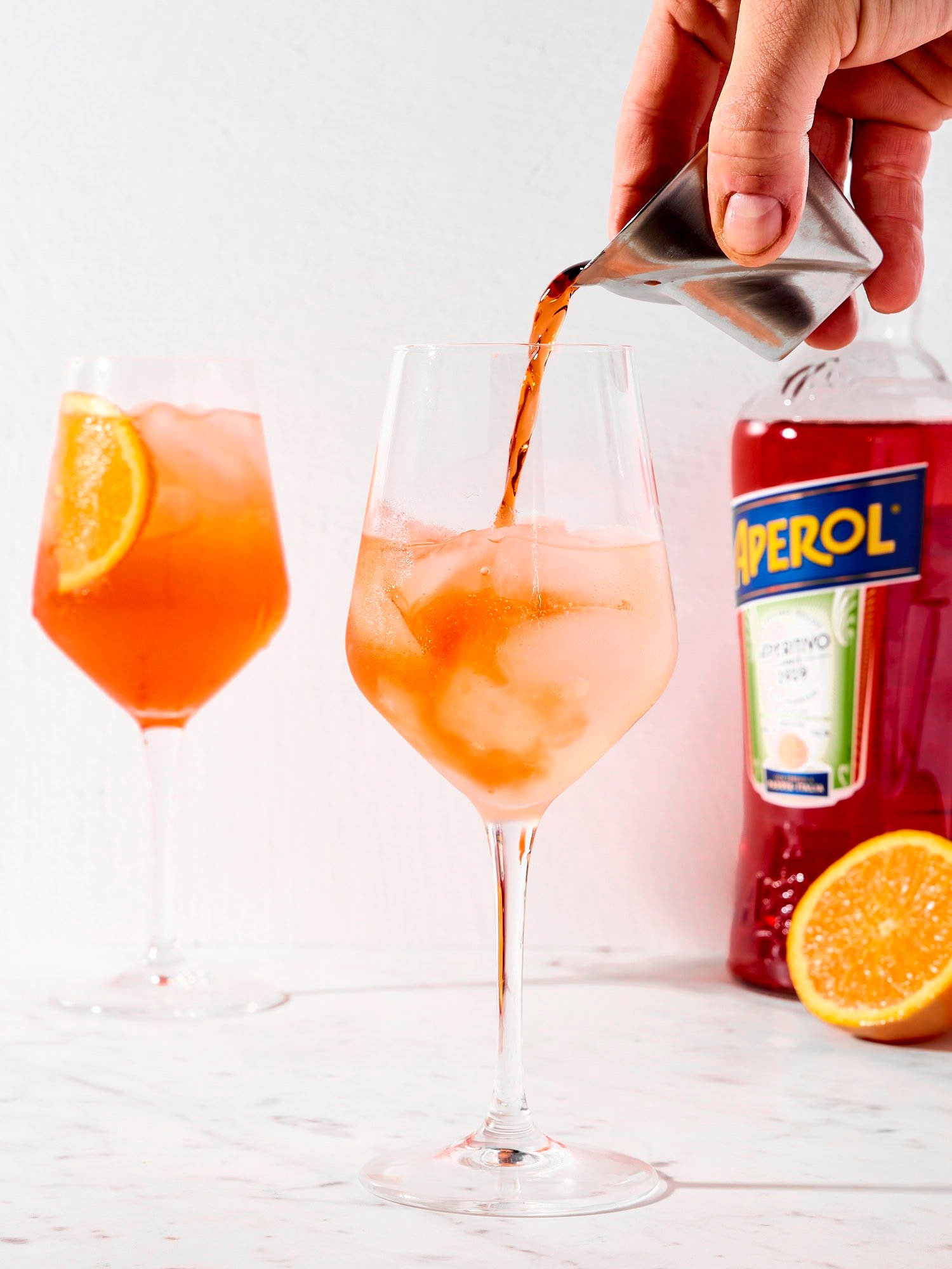Aperol being poured into wine glass with ice for an Aperol spritz.