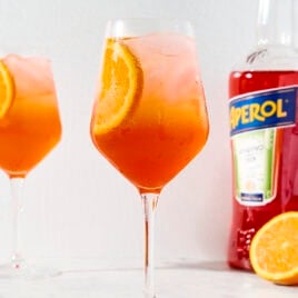 Wine glass with bright cocktail with slice of orange.