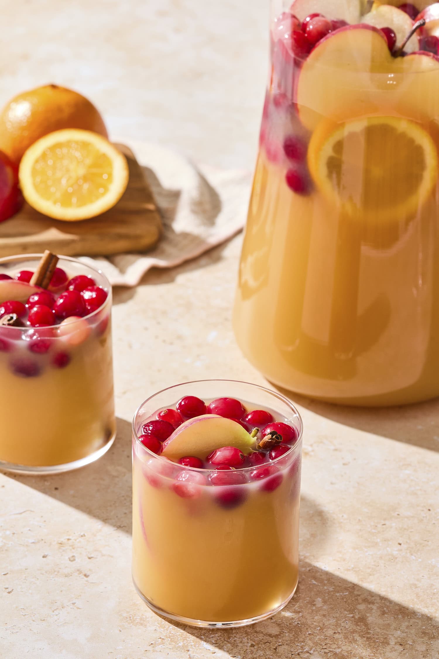 Two glasses with sangria with pitcher in background along with more garnishes.