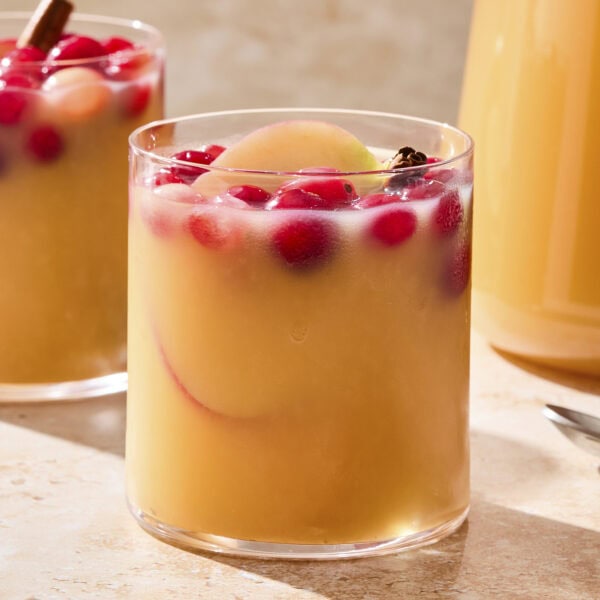 Two glasses of apple cider sangria garnished with cranberries and orange slices.