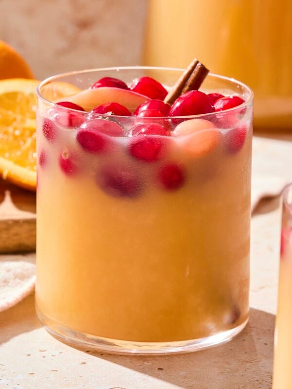 Glass filled with apple cider sangria with cranberries and a cinnamon stick as garnish.