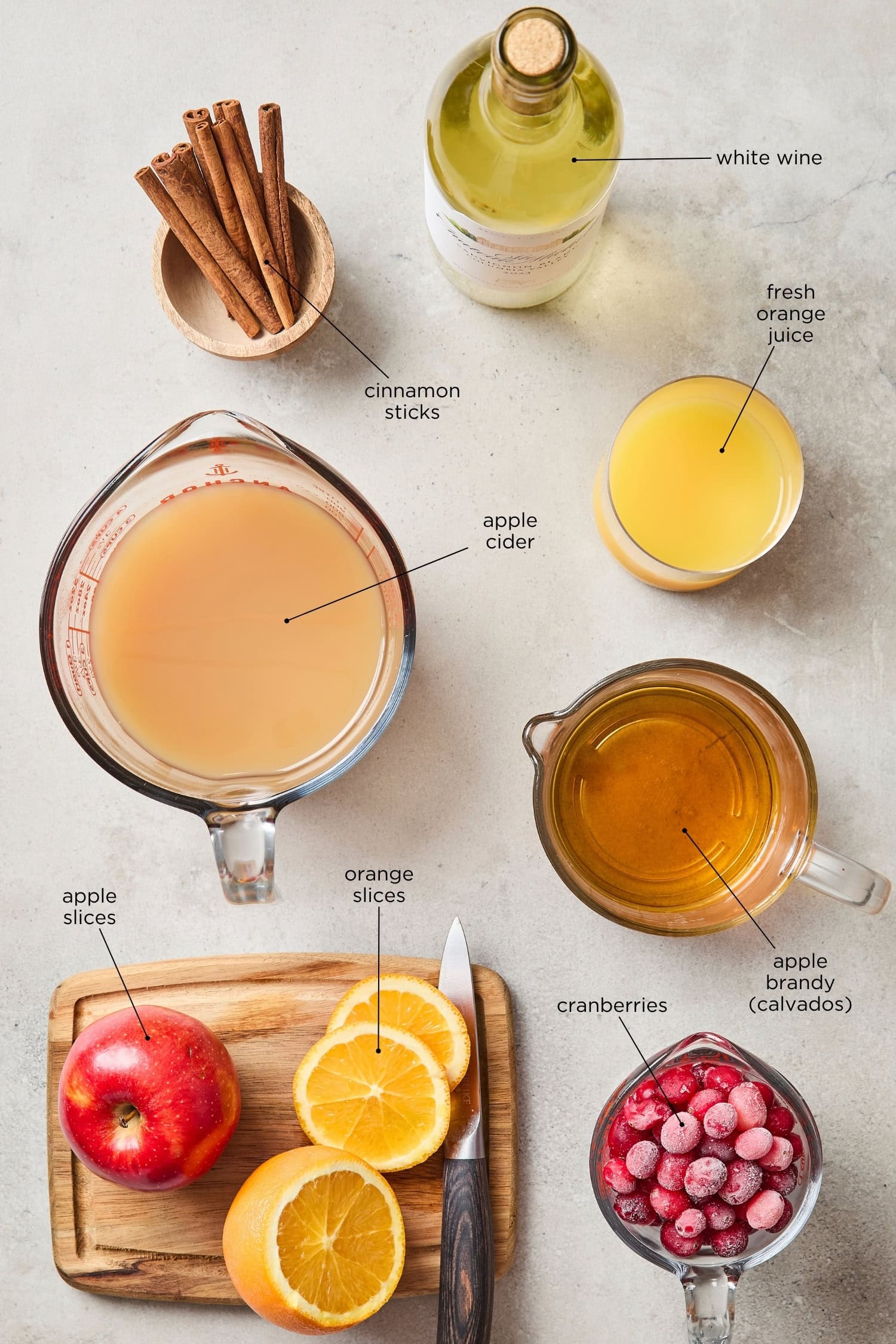 Concrete surface with ingredients needed for apple cider sangria with wine, brandy, apple cider, and more.