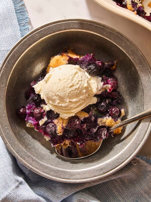 Metal bowl with serving of blueberry cobbler with scoop of ice cream on top.