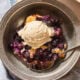 Metal bowl with serving of blueberry cobbler with scoop of ice cream on top.