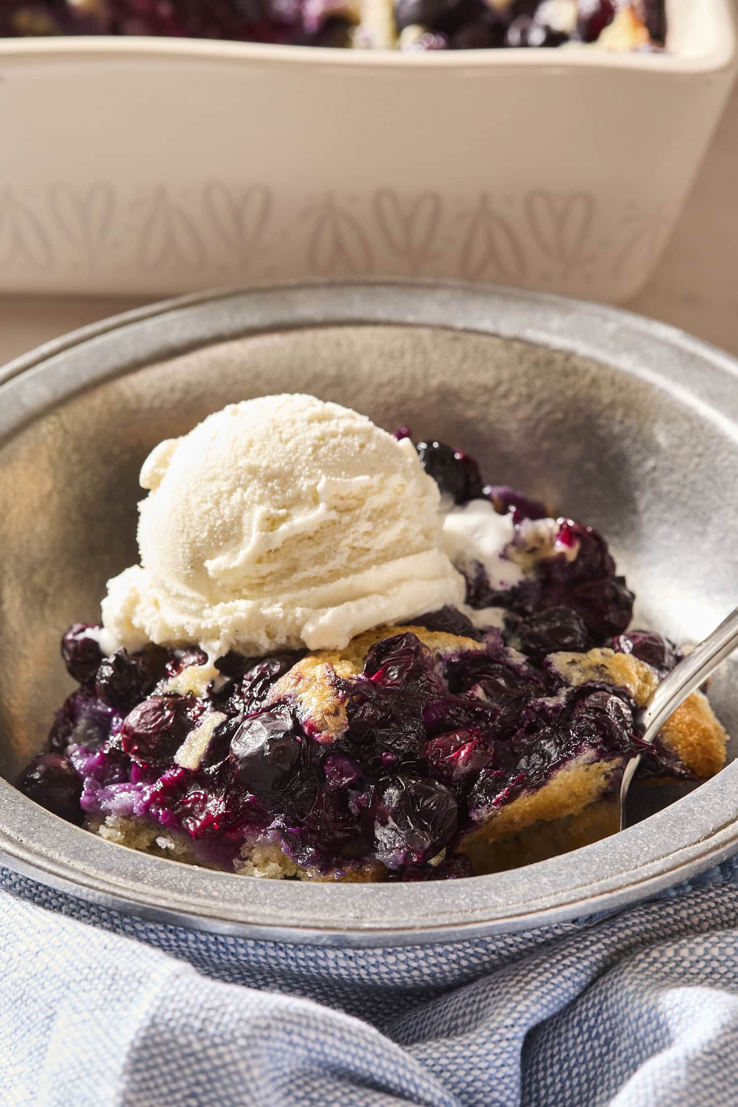 Scoop of blueberry cobbler in a metal bowl with ice cream on top.