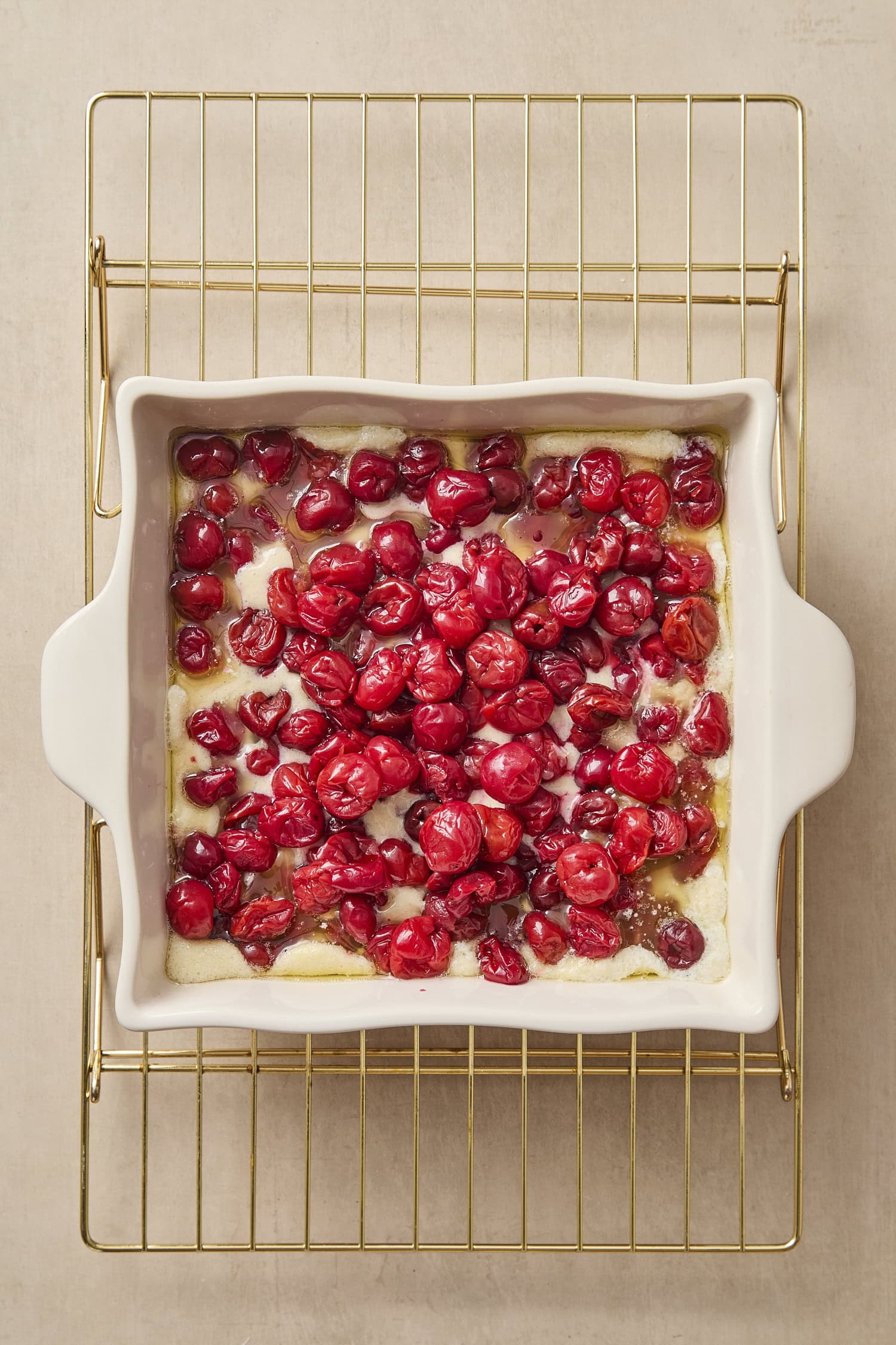 Pitted cherries on top of melted butter and batter in a baking dish.