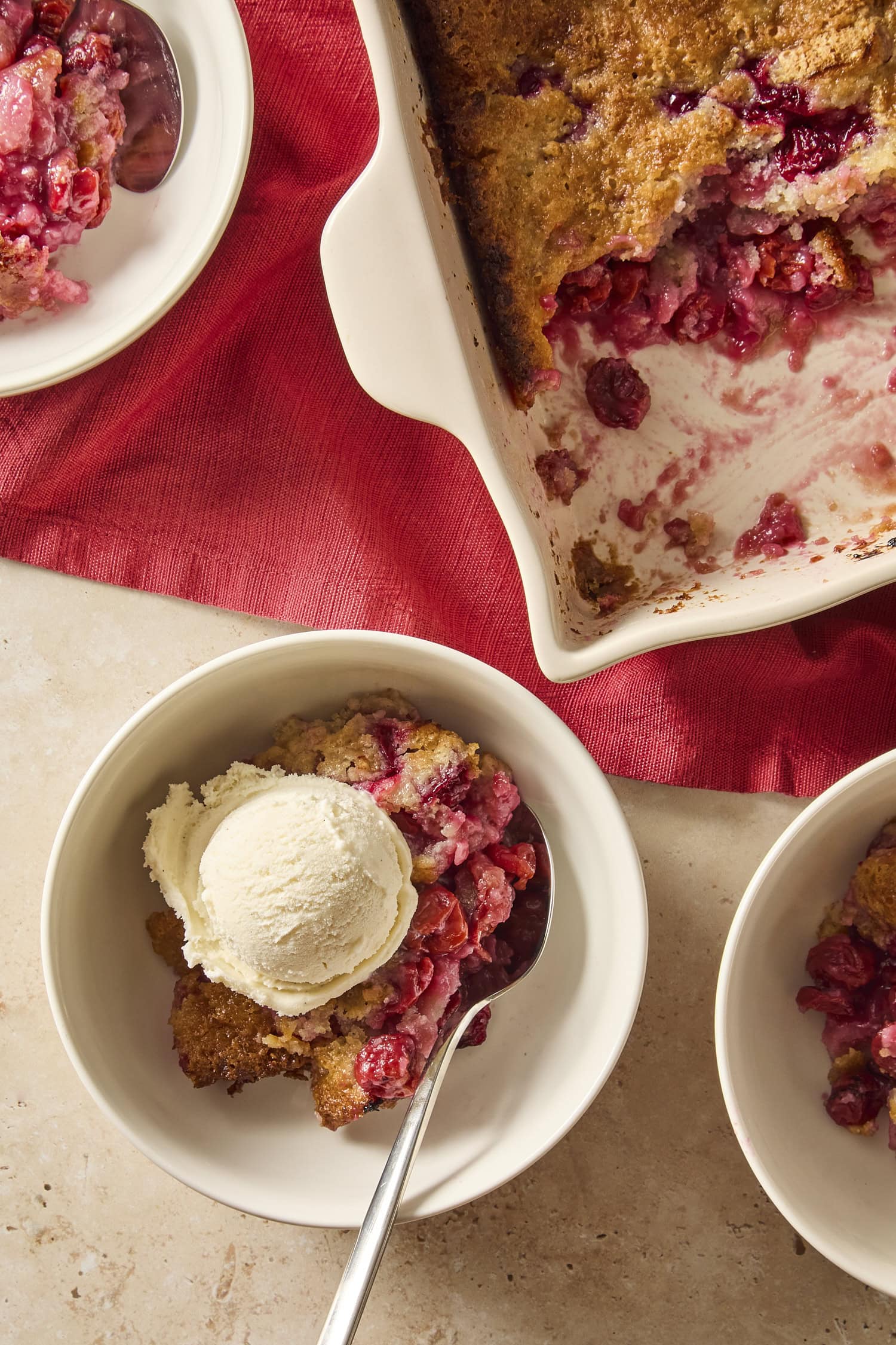 Bowl of cherry cobbler with scoop of ice cream on top with more cobbler in pan to the side.