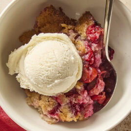 White bowl filled with serving of cherry cobbler with spoon.